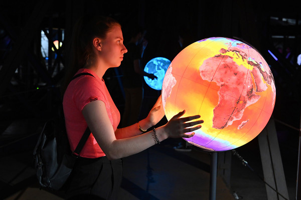 Eine Frau steht vor einem Globus in rot-gelber Farbe.