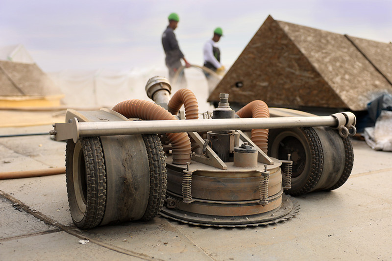 Im Vodergrung ist ein Roboter zu sehen, im Hintergrund zwei Arbeiter auf dem Gasometerdach.