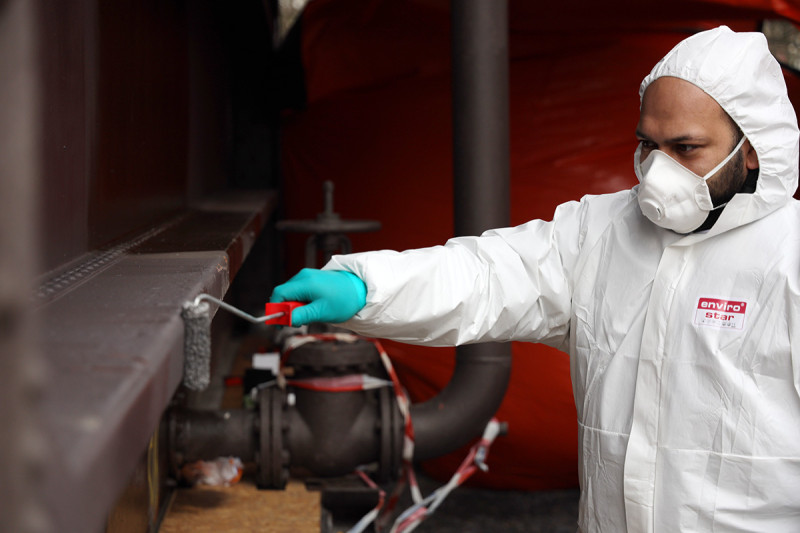 Eine graue Deckfarbe wird auf die Außenhülle des Gasometers gerollt.