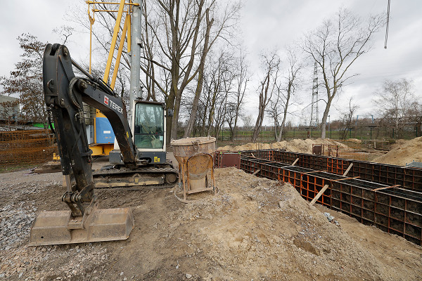 Ein Bagger vor den eingeschalten Streifenfundamenten der neuen Lagerhalle